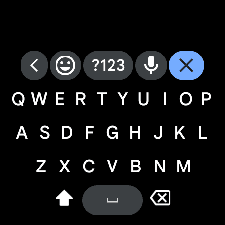 The Wear OS keyboard on a round watch, with emoji, numbers and microphone keys along the top